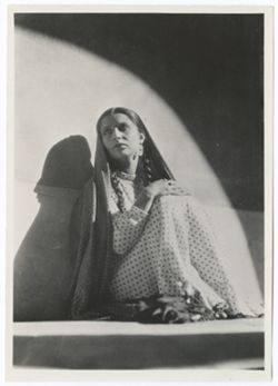 Item 0232.  Various shots of "Maria" (Isabel Villasenor) which cannot be placed in narrative sequence. Seated against a wall in a circle of light, her folded hands resting on her raised knees, head turned upward and toward the camera.