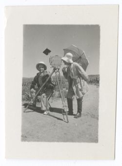 Item 1194. Eisenstein, seated by camera on tripod. Standing on opposite side of camera, a man carrying a parasol, wearing a floppy white hat and knee boots. See Item 300 above for same man.