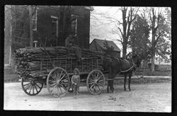 Horse drawn wagon loaded with tanbark, man sitting on top, small girl standing near