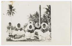 Item 06. Group of six young women wearing "sunflower" headdresses and seated on the ground.