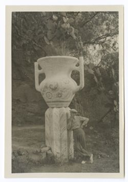 Item 0525. Tissé (?) leaning against fluted pedestal on top of which is a large two-handled urn. Urn and pedestal each ca. 6 feet high.