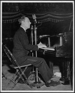 Hoagy Carmichael on stage and at a piano, playing and singing into microphones, 1930's.