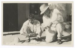 Item 0548. Kimbrough, right, kneeling beside an unidentified man reading notes or letters. Building in background.