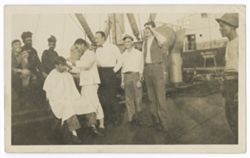 Item 0384. Group of men on ship's deck. Left, barber cutting man's hair, behind him, Hunter Kimbrough smoking a pipe.