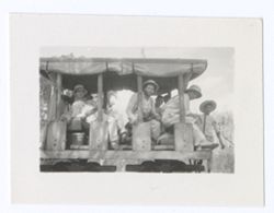 Item 1212b. - 1212c. Crew members on a railroad cart with rolled-up awnings on the sides. Eisenstein seated center, Tissé seated right. Kimbrough seated left.