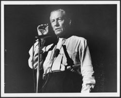 Hoagy Carmichael speaking into a microphone with a cigarette in his hand.