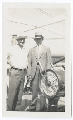 Item 0550. Kimbrough and two unidentified men standing by the wheel and engine room telegraph on the deck of a ship. Kimbrough, left, and man in business suit and fedora.