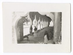 Indigenous woman standing in arch at entrance., Item 1202. - 1202a. Taken inside arcade, looking along it. Two men in pith helmets standing by column