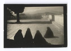 Item 0942. Four women draped in black seated in a large paved courtyard. See Items 278-278a above.