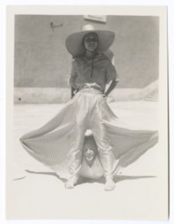 Item 0394a. Various shots of Eisenstein and a young woman wearing a checked culotte with wide leg in the courtyard of the Hacienda. Eisenstein is lying on the ground, looking out from between the spread legs of the girl's culotte.