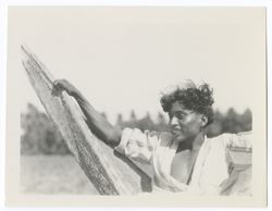 Item 0011. Young Indigenous man sitting in a hammock. Field and grove in background.