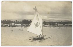 Item 70. Foreground, outrigger sailboat with stylized animal design on sail. Other boats and town in background.