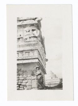 Item 1045. Another man in pith helmet and knee-high boots leaning against the southeast corner of the Iglesia, with the Caracol in background.