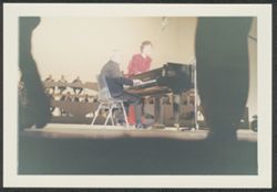 Hoagy Carmichael on stage playing the piano with an unidentified singer, with an orchestra in the background.