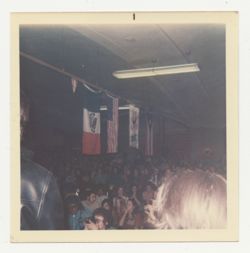 View of crowded room with flags hanging above