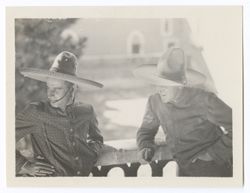 Item 0219. Two men wearing sombreros leaning against balcony rail, trees, courtyard and portion of Hacienda visible in background. Man at right is Julio Saldivar.