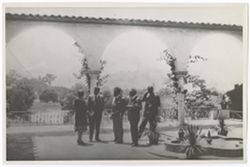 Item 0305. Group of people standing on a broad patio or terrace, with trees and hills in the background.