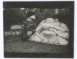 Item 1189. Man beside modern stone sculpture in garden. Kneeling beside sculpture.