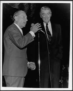 Hoagy Carmichael holding hands with James Stewart and speaking to an audience at an Indiana University Alumni Association event honoring Carmichael, Hollywood.