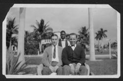Hoagy Carmichael and a man identified as George sitting in a rickshaw, with unidentified man behind them, surrounded by palm trees.