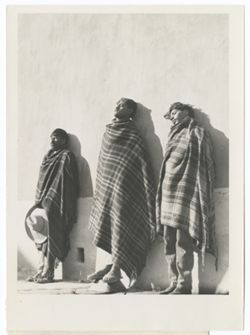 Item 0203. Three Indigenous men lined up against a wall. The one at far left holds his sombrero in front of himself against his legs, the one in the middle stands on a raised stone (?) the one at far right has his eyes closed and his head tilted to his right.