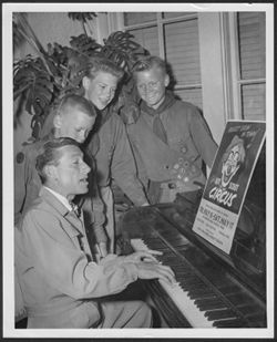 Hoagy Carmichael playing the piano for three young Boy Scouts.