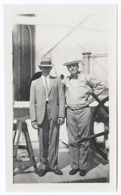 Item 0552. Kimbrough and two unidentified men standing by the wheel and engine room telegraph on the deck of a ship. Two unidentified men together.