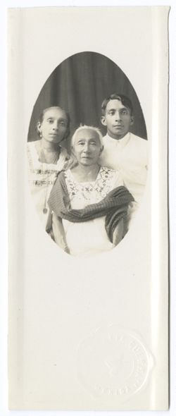 Item 0149. Oval portrait on glossy white stock. From left, young Indigenous woman, elderly Indigenous woman wearing narrow shawl (seated), young Indigenous man. Embossed seal on front: "Fotografia..Guerra.Mérida."