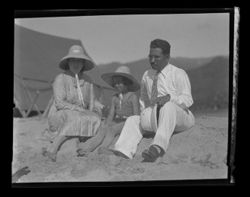 Item 0269. Unidentified woman, child and man sitting on rocks or sand, possibly at a beach.