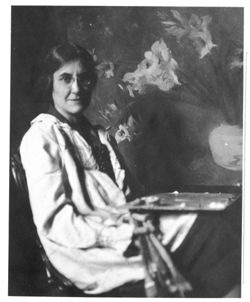 Marie Goth with palette, seated in front of painting