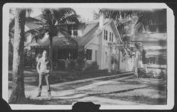 Hoagy Carmichael standing in the driveway near a house with palm trees in the background.