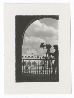Item 1098. - 1099a. Long shots of Cathedral and plaza, taken through archway with railing in front. Men and camera on tripod silhouetted in opening. See also Item 879 above. One man with camera. May be Tissé.