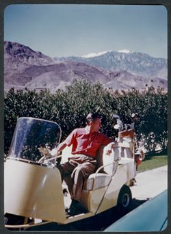 Hoagy Carmichael in golf cart, mountains in background.