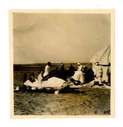 White couple on bed outside of tent being set up by group of Egyptian men