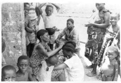 Woman plaiting girl's hair while Tapper waits to collect latex