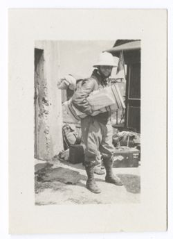 Item 1197. - 1197a. Eisenstein, in right and left profile, wearing pith helmet, leather jacket, and knee-high boots, with pack on his back and carrying a pillow and newspaper. Standing in front of adobe building with sacks, bags and trunks on ground around him.