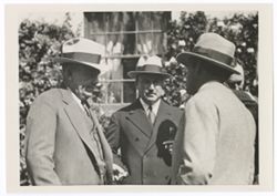 Item 0584. Three men in business suits standing in front of a building, a window of which is in center background. At far right, a fourth man is visible behind one of the other men.