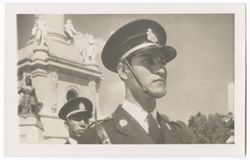 Item 50. Close-up of soldier in different-style hat and uniform from those seen in Postcards 42-49 in front of Monument. Another soldier, head only, visible behind the first.