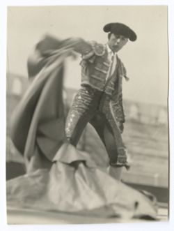 Item 0113. Liceaga in bullring, moving cape with his right hand. Full-figure shot, taken from in front and to his right. Portion of empty stands in background.