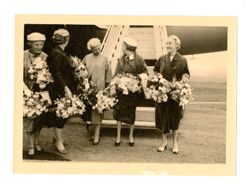 Women standing in front of airplane holding flowers