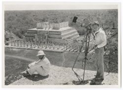 Item 0362. Eisenstein, seated left, and Alexandrov, standing beside camera, on top of the Castillo. Temple of the Warriors in the background.