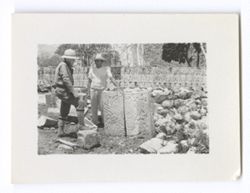 Item 1052a. Similar to Item 1052 above, but second unidentified man in a white hat and short-sleeved white shirt is standing directly beside stone block.