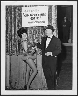 An unidentified woman and an unidentified man holding a sign, "As I said - 'Old Rockin Chair's Got Us,' Hoagy Carmichael."