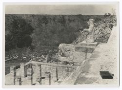 Item 0164. Taken from top of main stairway, Temple of the Warriors. Portion of colonnade at lower left, serpent head and stone figure at top of stairway at right. Briefcase lying at top of stairway. Foliage in background.