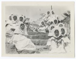 large building, probably a church, in background., Two files of young Indigenous women in "sunflower" headdresses seated and standing on either side of a flight of stone steps. Thatched fence or wall at extreme right