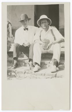 Item 55. Eisenstein, right, and unidentified man seated on low steps of building. Eisenstein holding a small stone head in his hands.