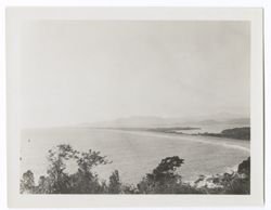 Item 0596. Shorelines of two adjoining lakes (?) with mountains in background. Probably taken from a hill, bushes and trees of which are visible in lower foreground.
