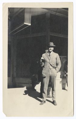 Item 0585. Unidentified man (Kimbrough?) standing in front of the entrance to the "[….]" You Café" holding a glass (of beer?).