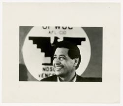 Cesar Chavez smiling in front of United Farm Worker flag
