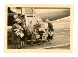 Women standing in front of airplane, holding flowers